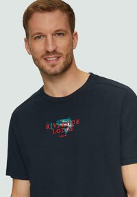 Navy blauwe t-shirt met een ronde halslijn, korte mouwen en een decoratief geborduurd "Riverside Lodge" logo in rood en teal.