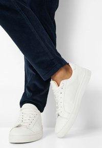 Hvide lædersneakers med lavt snit, rund tå og snørebånd foran, parret med mørkeblå kordfløjlsbukser.
