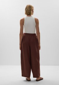 White sleeveless top paired with loose, rust-colored wide-leg pants. The pants feature an elastic waistband and fall just above the ankle.