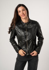 Schwarze Lederjacke mit rundem Kragen, Reißverschluss vorne und vertikalen Rippeneinsätzen an den Schultern. Verfügt über zwei seitliche Reißverschlusstaschen.