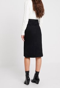 Musta mokkainen midi-hame, jossa on vartalonmyötäinen vyötärö, sivutaskut ja sileä pinta. Yhdistetty kiiltäviin mustiin nilkkureihin.