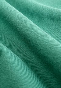 Gros plan sur un tissu bleu sarcelle doux avec une texture fine tricotée et de légers plis créant ombre et profondeur.