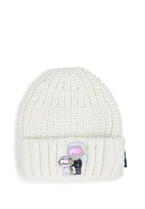 Bonnet blanc en tricot avec un bord replié, présentant un petit patch avec deux skieurs dessinés portant des lunettes de protection et tenant des bâtons de ski.