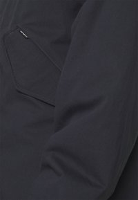 Marineblauwe jas met een textuur, voorzien van een subtiele diagonale naad en een zijzak met een klein logo-label.