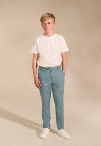 Hellblaue, maßgeschneiderte Hose mit strukturierter Oberfläche, kombiniert mit einem schlichten weißen T-Shirt und weißen Turnschuhen. Einfaches, modernes Design.