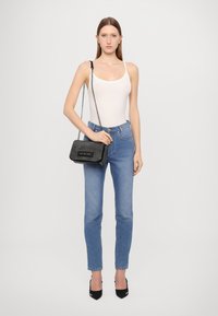 Canotta bianca, jeans a vita alta blu, borsa nera con tracolla a catena e tacchi neri. Texture liscia in tutto l'outfit.