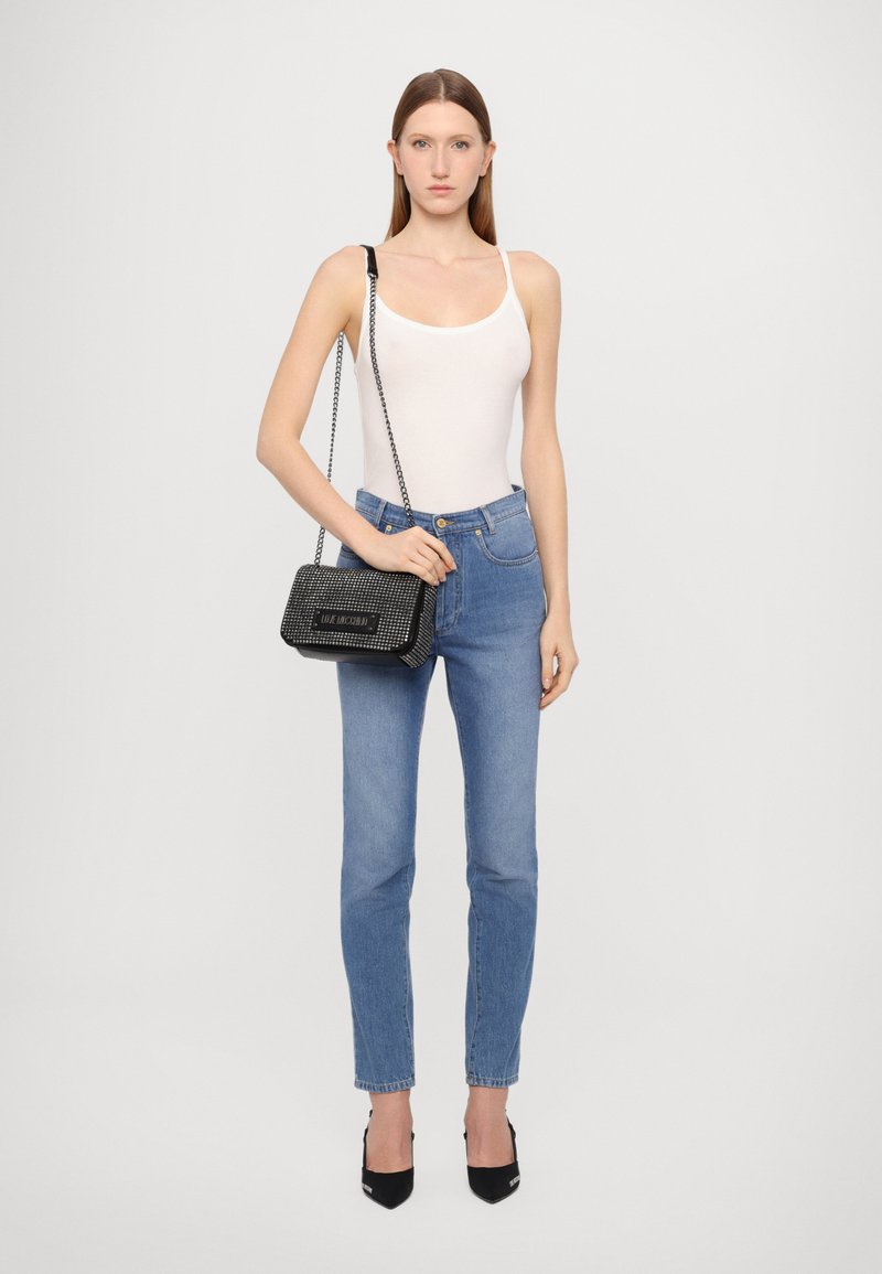 Canotta bianca, jeans a vita alta blu, borsa nera con tracolla a catena e tacchi neri. Texture liscia in tutto l'outfit.