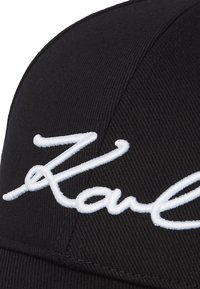 Black baseball cap featuring white embroidered text reading "Karl." Made from textured fabric with a curved brim.