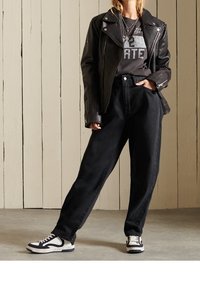 Cazadora negra de cuero estilo motero sobre una camiseta gris con gráfico, combinada con vaqueros negros de cintura alta y zapatillas negras y blancas.