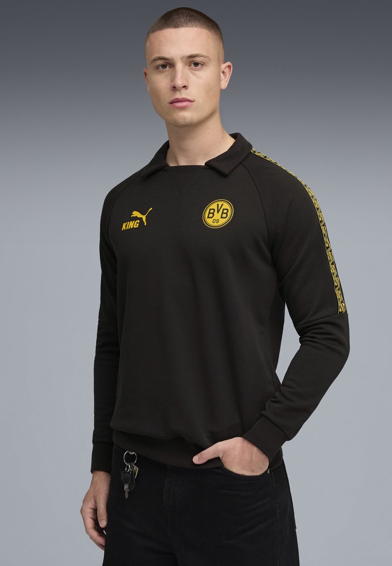 Sort sweatshirt med krave, der har et gult logo og tekst på brystet og langs ærmerne. Lange ærmer og ribbede manchetter.