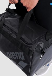 Bolsa de viaje negra con una tela texturizada, con asas reforzadas duales y un gran compartimento con cremallera. Logotipo impreso de forma destacada en el lateral.