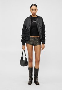 Μαύρο σατέν μπουφάν bomber, μαύρο κοντομάνικο μπλουζάκι με το κείμενο "Juice", μεταλλιζέ σορτς με κουμπιά, μαύρες μπότες που φτάνουν μέχρι το γόνατο και μαύρη τσάντα ώμου.