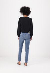 Melna garām piedurknēm augšdaļa ar apaļu kakla izgriezumu, apvienota ar gaiši ziliem slaidajiem džinsiem ar aizmugurējām kabatām un diskrētu logotipa detaļu.