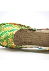 Espadrille jaune coloré avec des motifs de feuilles vertes, extérieure en jute tressé, bordure tressée et semelle intérieure en corde texturée.