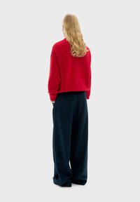 Rode gebreide trui met een cropped ontwerp, gecombineerd met losse, donkerblauwe broek. Zachte textuur en een ontspannen silhouet.
