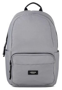 Rucsac gri cu textură netedă, formă curbată, buzunar frontal cu fermoar și patch cu marcă. Are o mânere superioară și bretele reglabile.