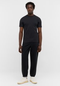 T-shirt noir à manches courtes associé à un pantalon de jogging noir et des baskets blanches. Design simple avec une coupe décontractée et un minimum de détails.