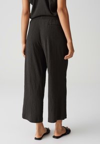 Pantalons larges noirs, texturés, avec une taille élastique et une poche arrière, associés à des sandales plates noires.