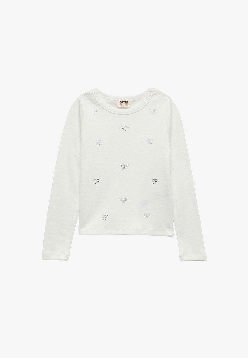 Pitkähihaisessa, valkoisessa puuvillapaidassa on pyöreä pääntie, jossa on pieniä mustia solmukuvioita tasaisesti jakautuneena etuosassa ja pehmeä rakenne.