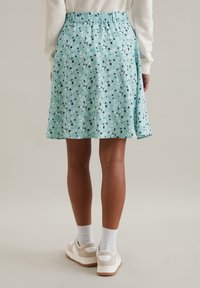 Une jupe vert menthe avec un motif floral, dotée d'une taille élastique. Associée à des chaussettes blanches et des baskets beiges.