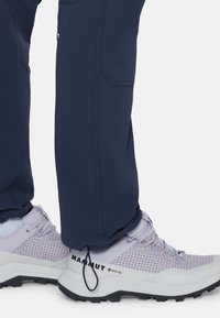 Marineblauwe broek met omgeslagen pijpen bij de enkel, gedragen over lichtpaarse Mammut Gore-Tex wandelschoenen met zwarte robuuste zolen en witte sokken.