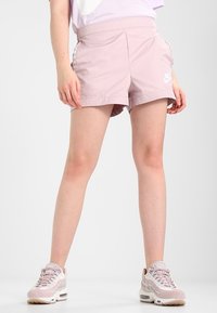 Helle rosa Nike Sportshorts mit elastischem Bund, seitlichen Streifen und Logo-Details. Glattes Material und knielange Schnittform.