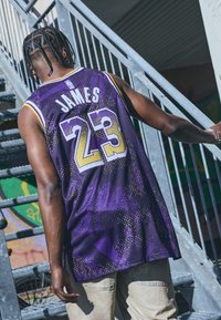 Maglia da basket viola con accenti bianchi e gialli, numero 23 e "JAMES" sul retro, realizzata in un tessuto testurizzato e patternizzato.