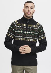 Schwarzer Pullover mit Reißverschluss und geometrischem, gemustertem Design in Grün, Braun und Weiß. Strukturierter Strickstoff mit gerippten Bündchen.