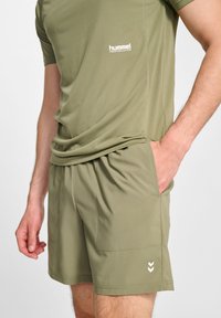 Olivgrön träningslinne och shorts-set, med en figurnära design och fuktavledande tyg. Inkluderar sidofickor och logodetalj.