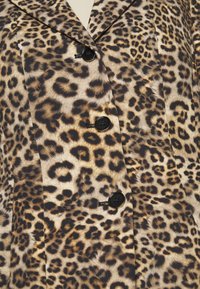 Tissu à imprimé léopard avec boutons noirs sur un manteau ou blazer sur mesure, montrant les détails du col et de la fermeture avant.