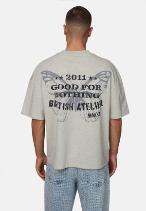 Szara, oversizeowa koszulka z dużą grafiką motyla i napisem na plecach. Krótkie rękawy, okrągły dekolt, miękka tekstura materiału.