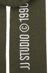 Olive green knitted scarf featuring white embroidered text reading "© 1990 studio," with soft, textured fabric and straight edges.