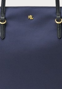 Ναυτικό μπλε τσάντα ώμου φτιαγμένη από υφασμάτινη υφαφή με μαύρες δερμάτινες λαβές. Διαθέτει χρυσό λογότυπο και στρογγυλές μεταλλικές λεπτομέρειε�ς.