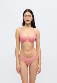Σετ ροζ δαντελωτού εσωρούχου που περιλαμβάνει ένα σουτιέν με ενίσχυση και κυματιστά άκρα με γεωμετρικά σχέδια, συνδυασμένο με ένα αντίστοιχο σλιπ με λεπτομέρειες με λουράκια.
