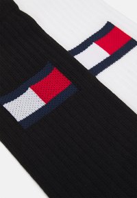 Ropa de punto en blanco y negro con una tela texturizada. Un lado presenta un logo con rectángulos rojos, blancos y azules.