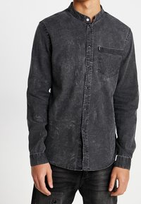 Camicia button-up in denim nero con colletto alla francese, maniche lunghe, taschino frontale e una finitura sfumata e testurizzata.