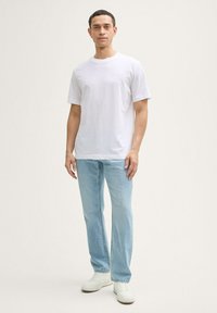 Hvid bomulds T-shirt med rund hals, parret med lyseblå jeans. Outfittet fuldendes med hvide sneakers. Minimalistisk design.