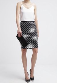 Black and white patterned pencil skirt paired with a white tank top and black high heels; woman holding a black clutch. Simple design.