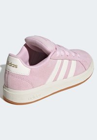 Baskets en daim rose avec des accents blancs, dotées d'un col rembourré, de trois bandes blanches et d'une semelle en caoutchouc marron. Logo "adidas" sur le talon.