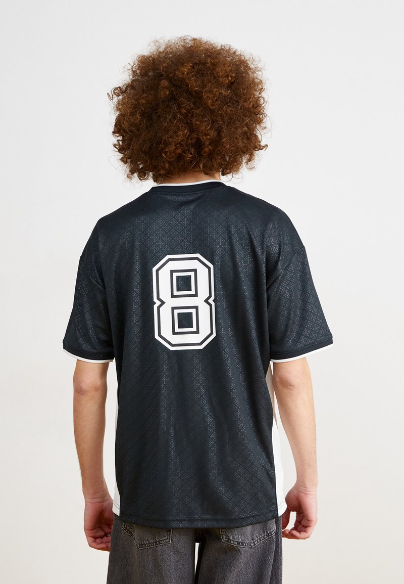 Camiseta negra con un patrón de diamantes texturizado, acentos blancos y un gran número 8 blanco en la parte posterior. Mangas cortas y diseño de cuello redondo.