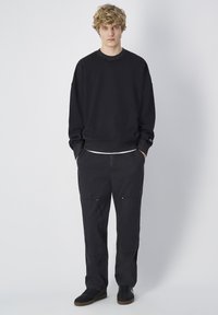 Sudadera negra con cuello redondo y hombros caídos, combinada con pantalones cargo negros que tienen bolsillos y un ajuste relajado. Zapatillas negras.