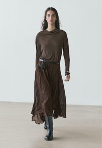 Brown long-sleeve shirt with a draped neckline, paired with a brown polka dot skirt and knee-high dark boots. Belted pouch detail included.