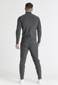 Grå randigt herrmjukisset med en figursydd långärmad topp och avsmalnande byxor, tillverkade av mjukt tyg med ribbad struktur.