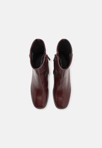 Bottes basses en cuir bordeaux à texture lisse, bout arrondi, et fermeture éclair latérale. Intérieur doté d'une doublure douce pour le confort.