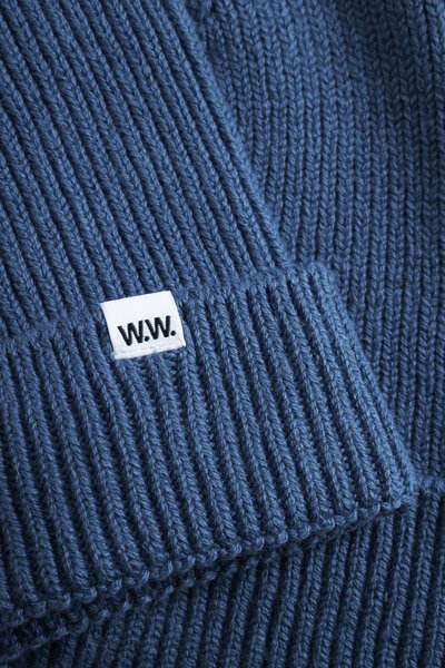 Sinine kootud beanie ribatud tekstuuriga. Omab väikest valget sildit, millel on musta värviga õmmeldud "W.W.". Paks lõng loob hubase välimuse.