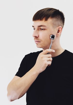 Ansiktsruller i bruk, kromhåndtak, svart rullhode. Subjektet har på seg en svart skjorte, kort frisyre og naturlig hudtone.