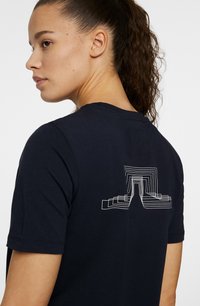 Svart bomulls-t-shirt med ett vitt geometriskt linjemönster på ryggen. Korta ärmar och rund halsringning, slät textur.