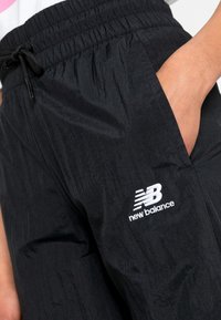 Zwarte lichtgewicht joggerbroeken met een elastische tailleband, een externe trekkoord, zijzakken en een witte geborduurde "New Balance"-logo.