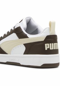 Brązowe i białe trampki wykonane z materiałów skórzanych i syntetycznych. Posiadają logo PUMA, teksturowane akcenty oraz wyściółkę dla większego komfortu.