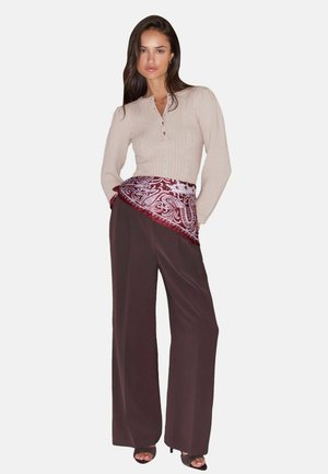 Woman wearing beige ribbed long-sleeve top, brown wide-leg pants, burgundy paisley scarf tied around waist, and black open-toe heels.